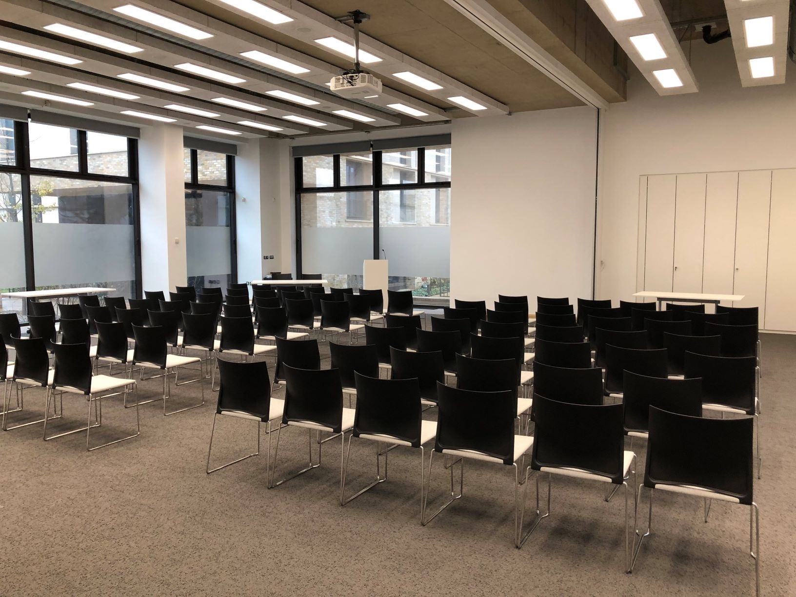 Photograph showing the lecture-style layout of Sanders Hall - a room with seven rows of chairs facing a lectern and projector screen on the end wall.